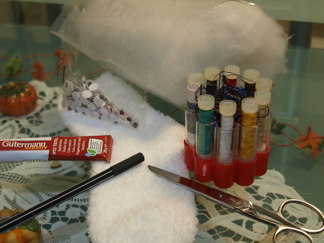 Materialien zum Basteln einer Geister-Socke: Eine weiße Socke, eine Schere, Textilkleber, Füllwatte, Nadel, Garn und Wackelaugen.