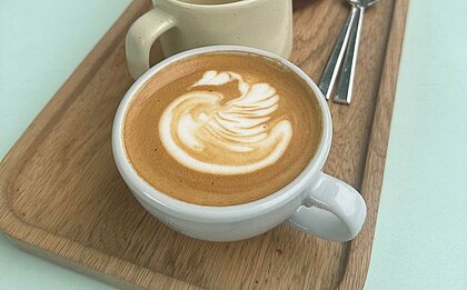 Auf dem Bild sieht man eine Kaffee Tasse gefüllt mit einer Kaffeespezialität samt Latte Art