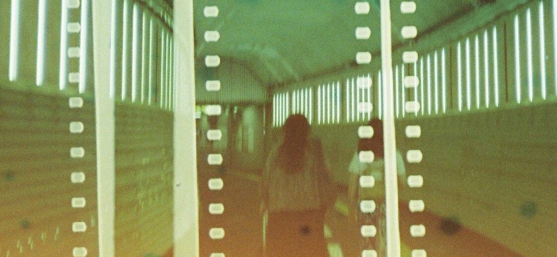 Auf dem Bild ist eine Frau von hinten fotografiert. Sie ist in einem Tunnel. Auf dem Bild liegt ein Filter, der Filmstreifen darstellt. Das Bild ist in Grünfarben getaucht. 