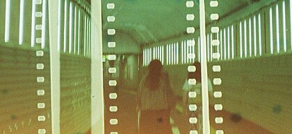 Auf dem Bild ist eine Frau von hinten fotografiert. Sie ist in einem Tunnel. Auf dem Bild liegt ein Filter, der Filmstreifen darstellt. Das Bild ist in Grünfarben getaucht.