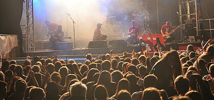 Zu sehen ist eine Festivalbühne mit Menschen vor und auf der Bühne