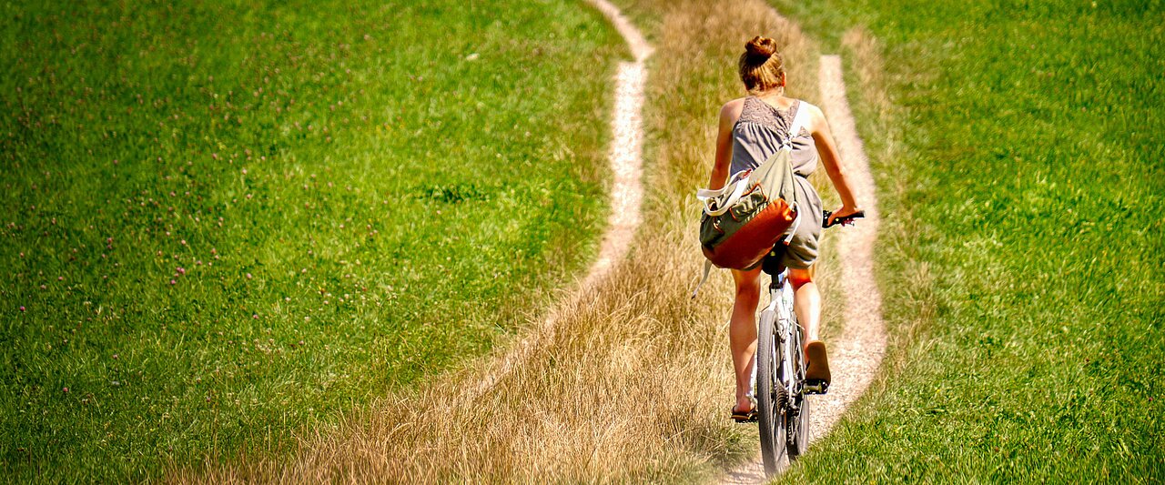 Frau auf dem Fahrrad, fährt über einen Feldweg