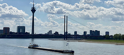Auf dem Foto sieht man die Düsseldorfer Skyline bei gutem Wetter mit einem Boot im Vordergrund auf dem Rhein
