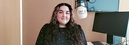 Auf dem Foto ist Elif Benli zu sehen. Sie steht neben einem Mikrofon und lächelt in die Kamera.