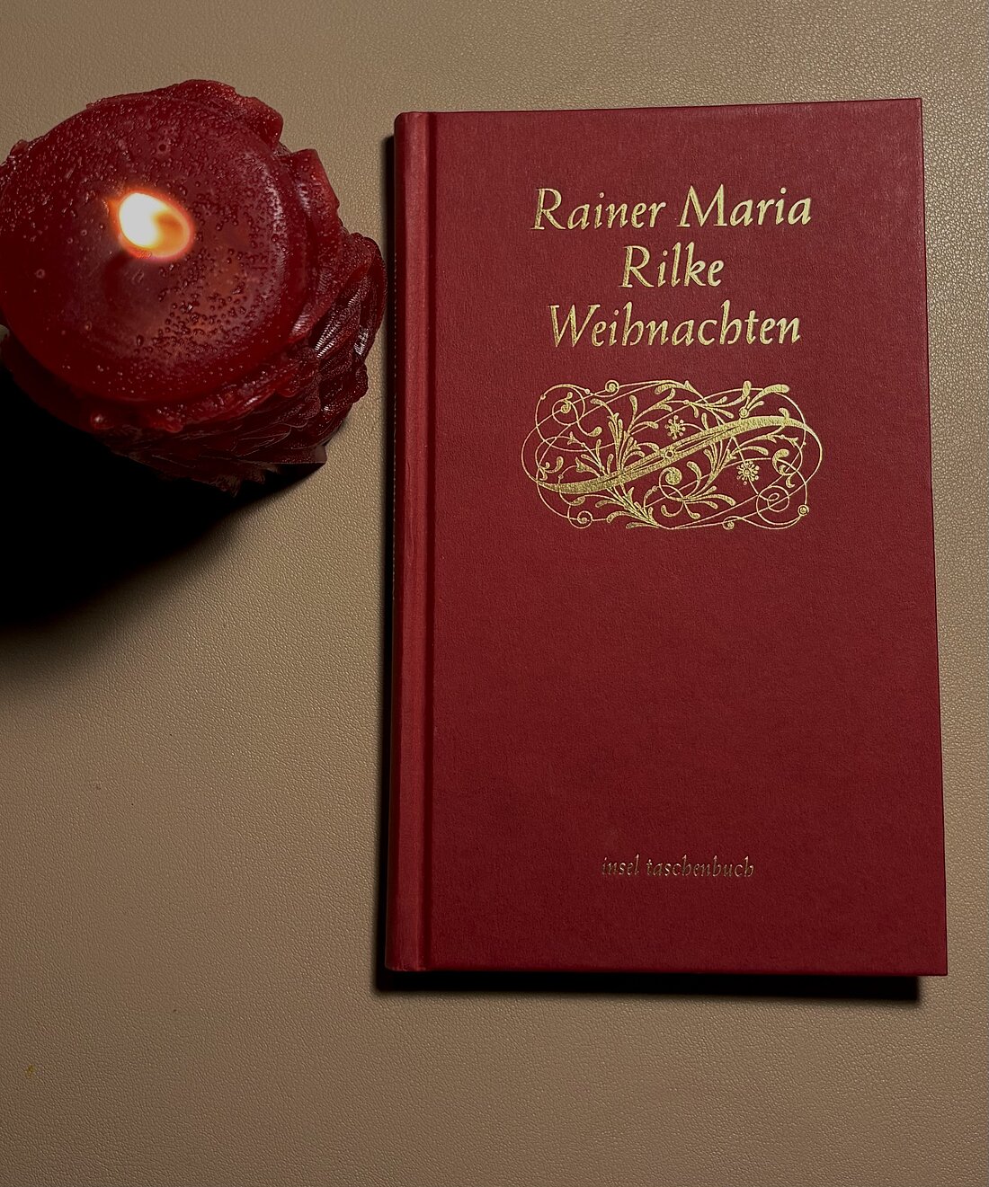 Auf diesem Bild sieht man das Buchcover von Rainer Maria Rilke: Weihnachten und daneben steht eine rote Kerze 
