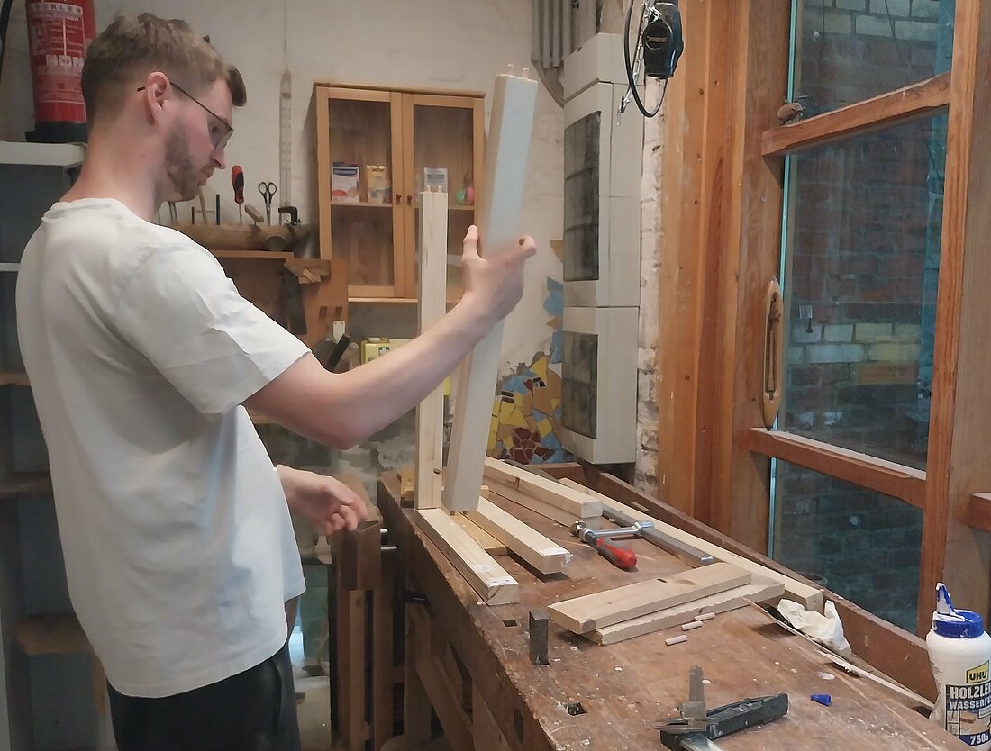 Für 20€ in Monat steht die Holzwerkstatt jeden zur freien Verfügung. (Fotografin: Katharina Dvorak) Ein Mann arbeitet an einer Werkbank. Er leimt Hölzer für einen Rahmen aneinander.