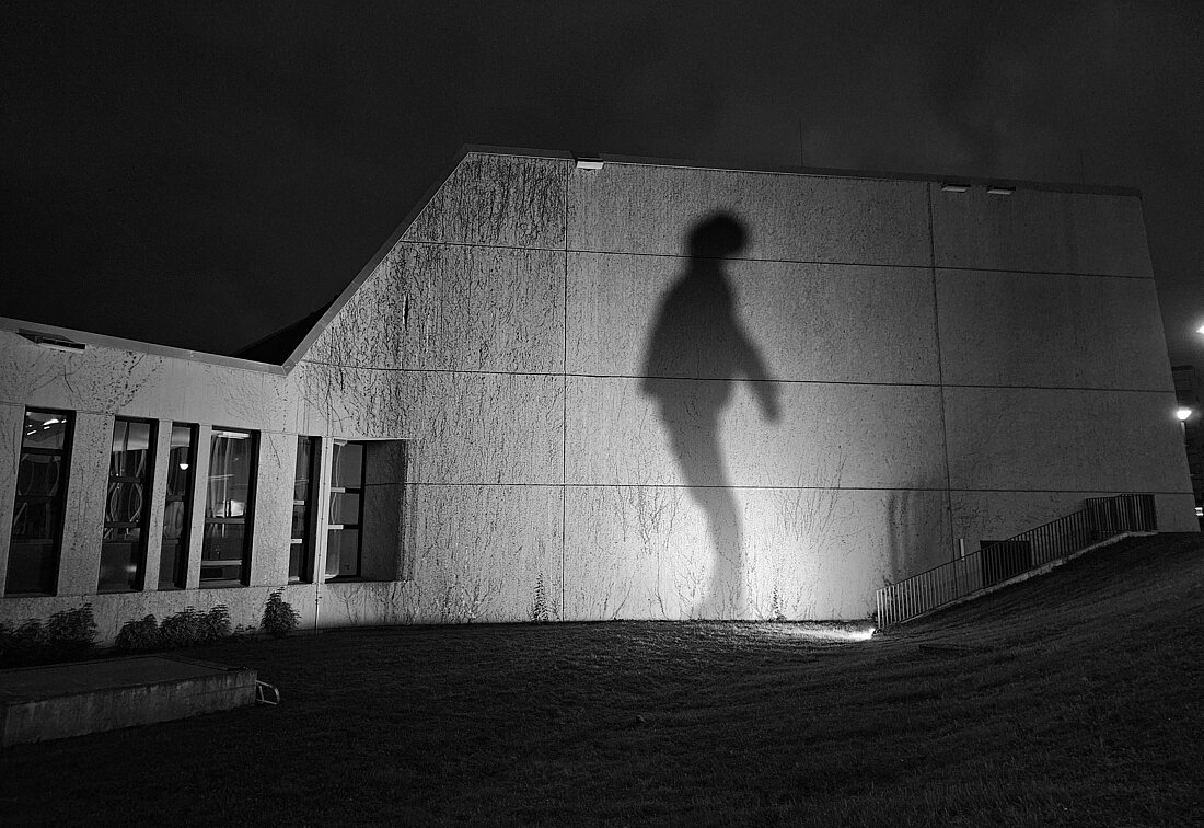 Ein Schwarz-Weiß Bild von einem Schatten an einer Gebäudewand. Der Schatten scheint Hoffnung auszudrücken. 