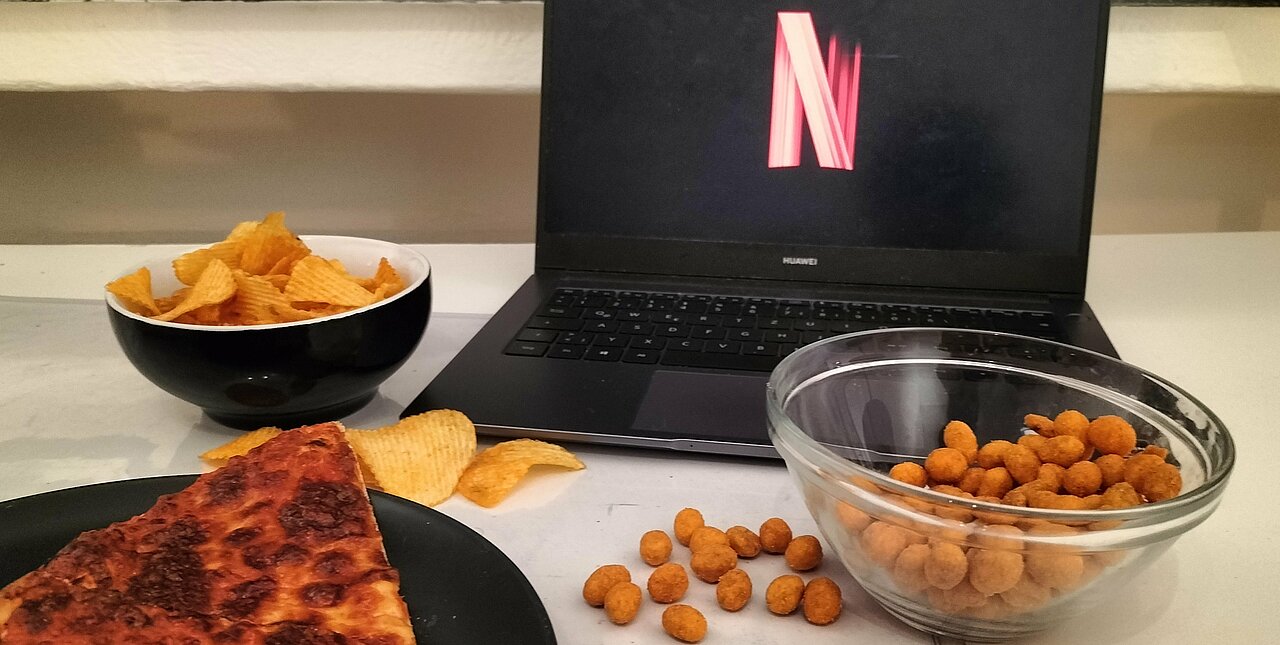 Auf dem Foto sind Pizzastücke, Chips und Nic Nacs vor einem Laptop mit Netflix Logo zu sehen.