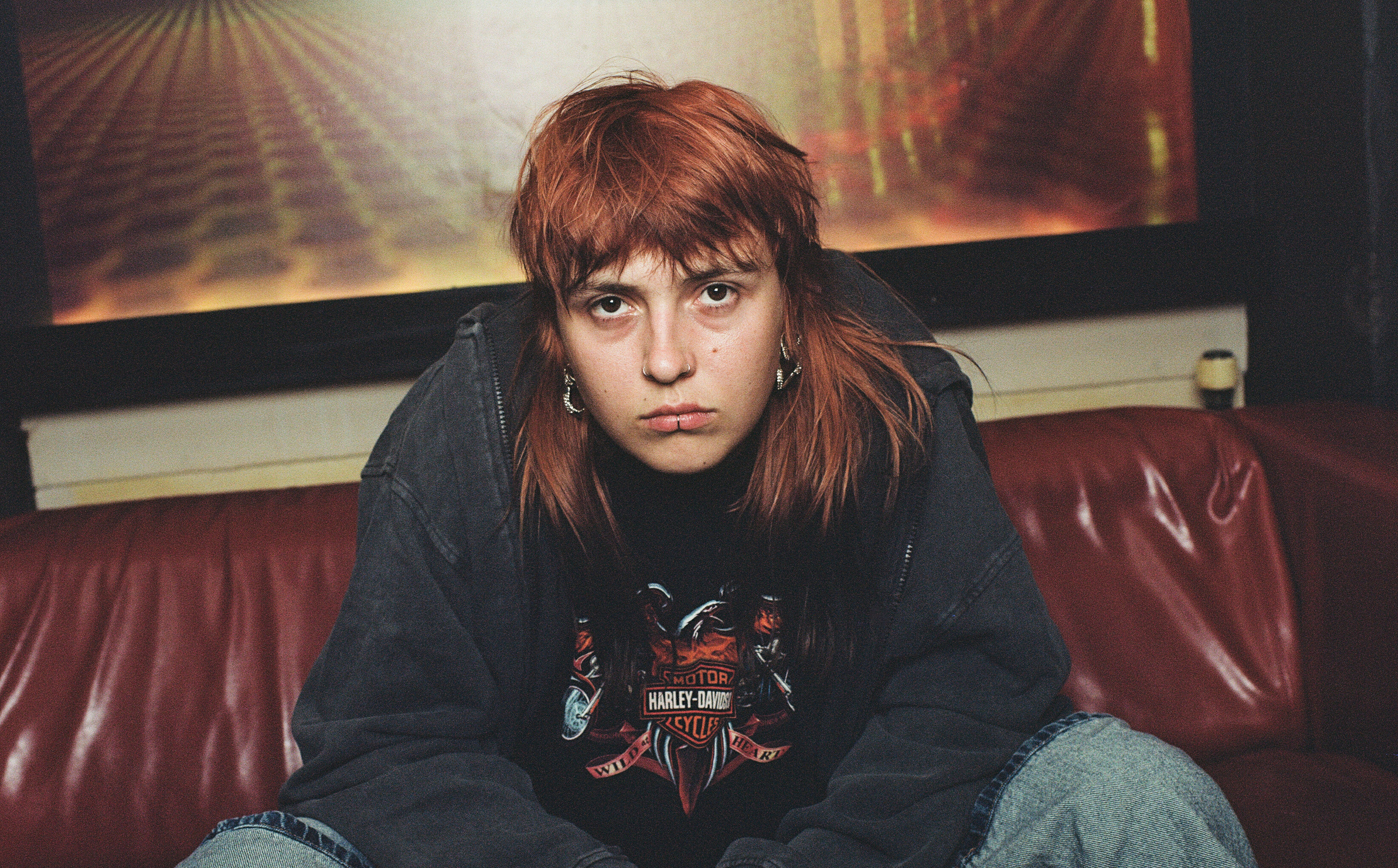 Mit ihrer neuen EP betont Leila, wie Leistungsanforderungen bei der Arbeit, Klimawandel und politische Entwicklungen Druck bei der jungen Generation erzeugen (Foto: Simon Habegger). Die Künstlerin Leila sitzt auf einem Sofa und schaut in die Kamera.