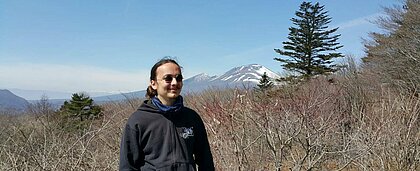 Eindrücke aus einer japanischen Berglandschaft (Foto: Gunnar Hütz) Man sieht einen Studierenden der HHU vor einer japanischen Berglandschaft. Die Sonne scheint ihm ihn ins Gesicht und er lächelt zufrieden.