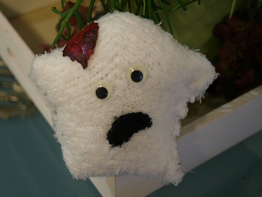 Eine kleine Geister-Socke mit Wackelaugen und einem roten Blatt auf dem Kopf.