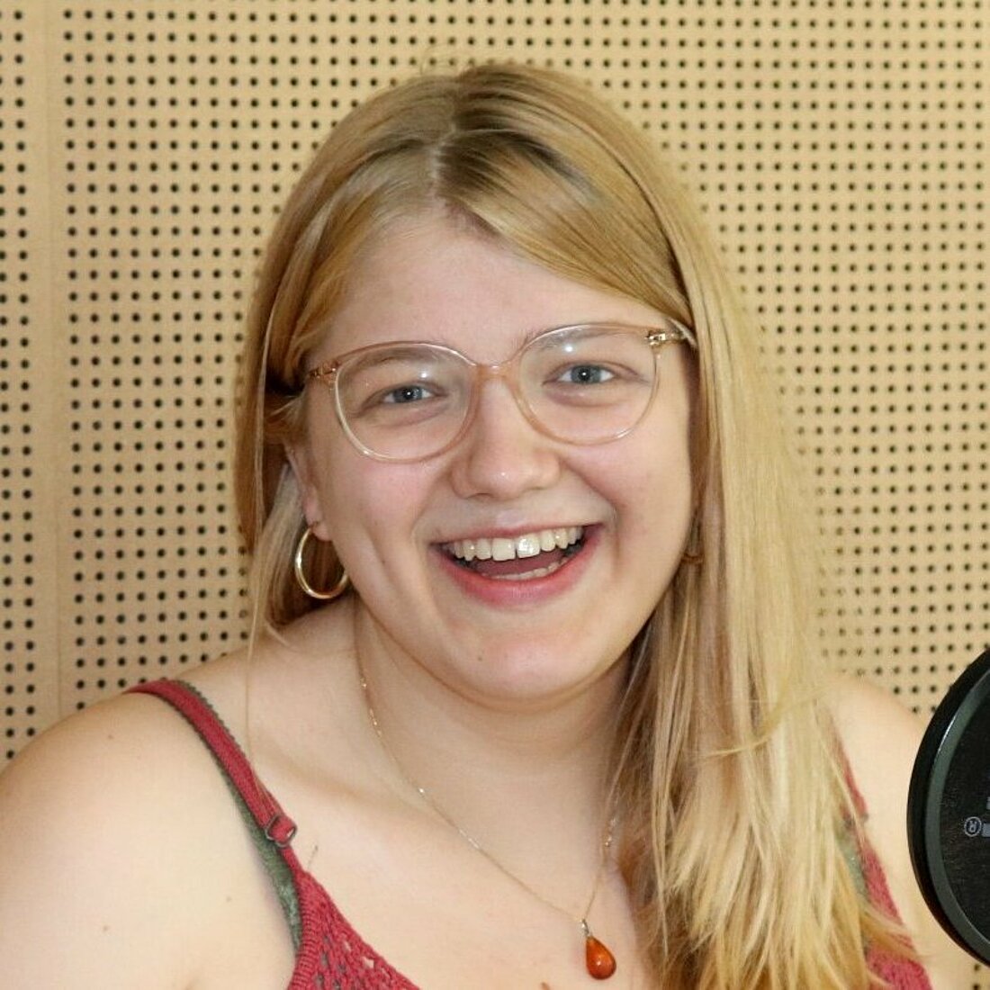 Eine junge Frau steht im Radio-Studio und lacht in die Kamera.