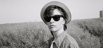 Zu sehen ist eine junge Frau mit Sonnenbrille und Hut