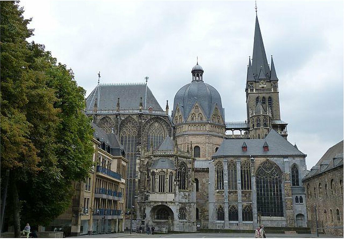 Zu sehen ist ein altes, gothisches Bauwerk unter wolkigem Himmel. Es zeigt der Aachener Dom.