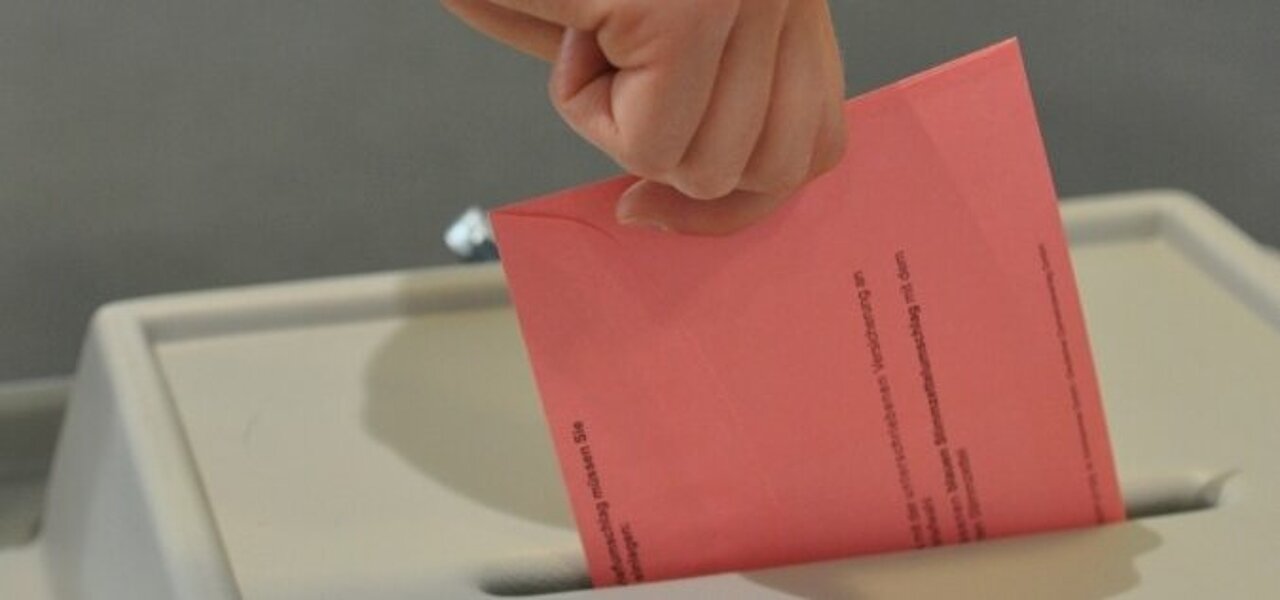 Ein Wahlschein wird in die Wahlurne im Wahllokal eingeschmissen.