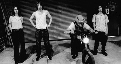 Auf dem Foto sieht man die Cameron Winter und seine Band Geese. Sie stehen vor einer Garage, einer sitzt auf einem Motorrad. Das Foto ist Schwarzweiß (Foto:Lewis Evans)