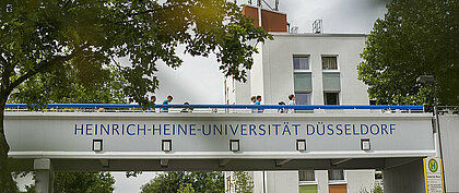 Leben kehrt auf den Campus der Heinrich Heine Universität zurück. (Foto: HHU/Ivo Mayr) Zu sehen sind Studierende auf einer Fußgängerbrücke des Campus