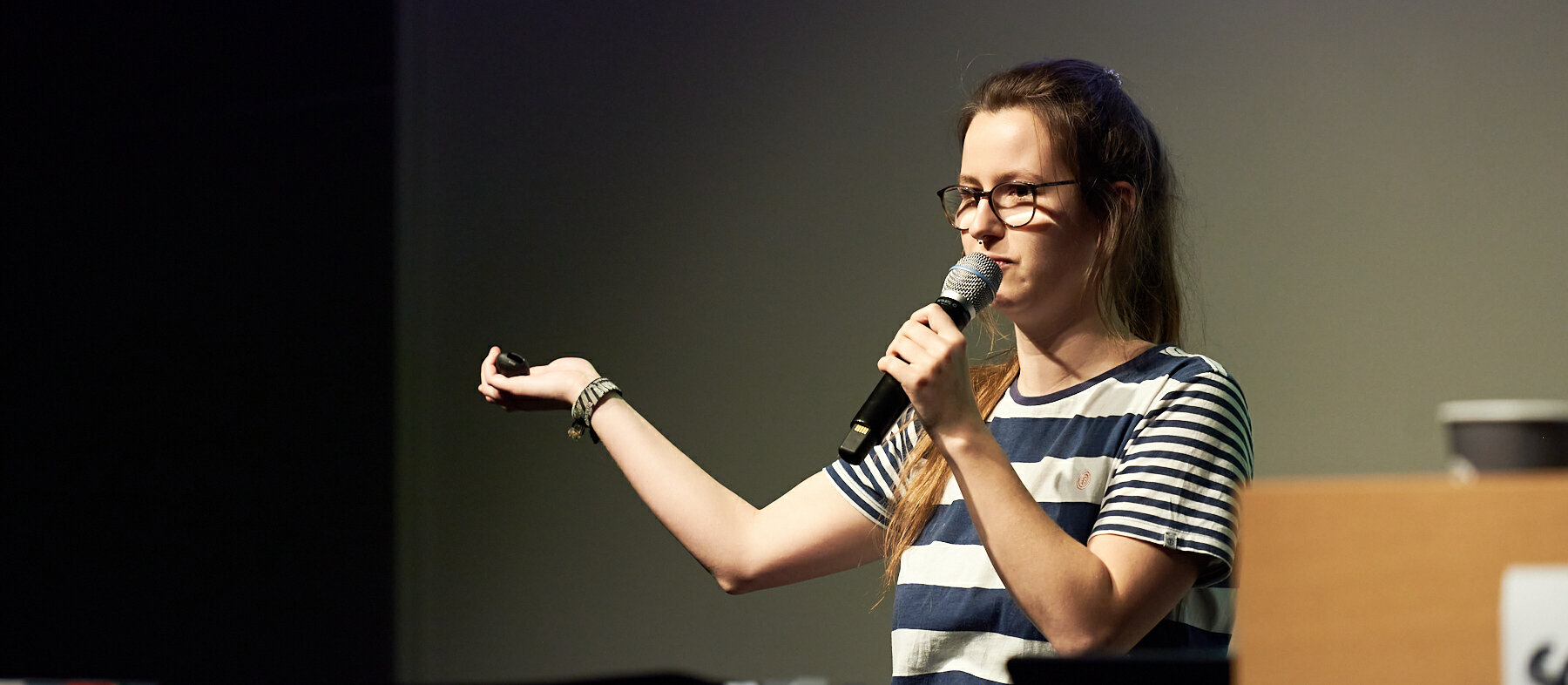 Anna Hülkenberg auf der Bühne bei einem Slam. Sie trägt einem gestreiftes T-Shirt und hält ein Mikrofon in der Hand.