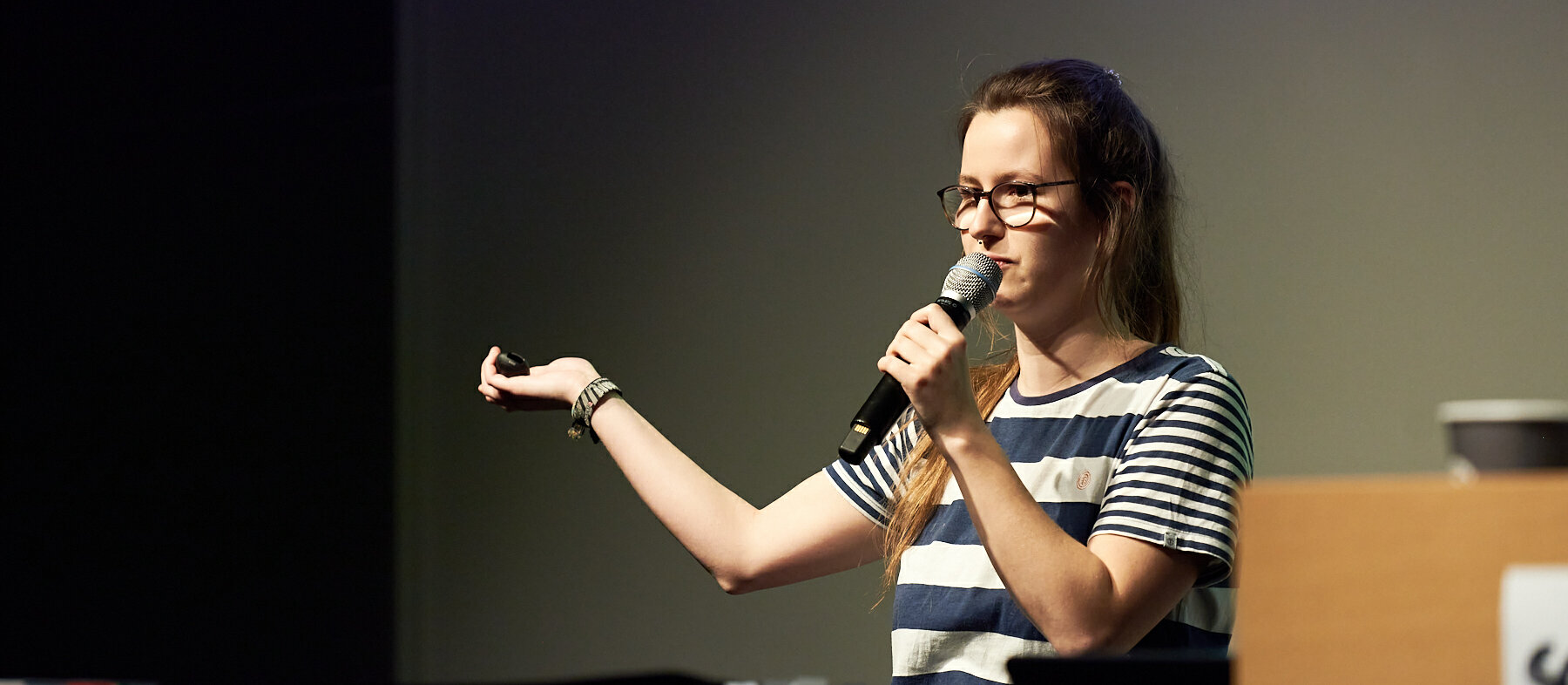 Anna Hülkenberg auf der Bühne bei einem Slam. (Foto: Klangblende) Anna Hülkenberg auf der Bühne bei einem Slam. Sie trägt einem gestreiftes T-Shirt und hält ein Mikrofon in der Hand.