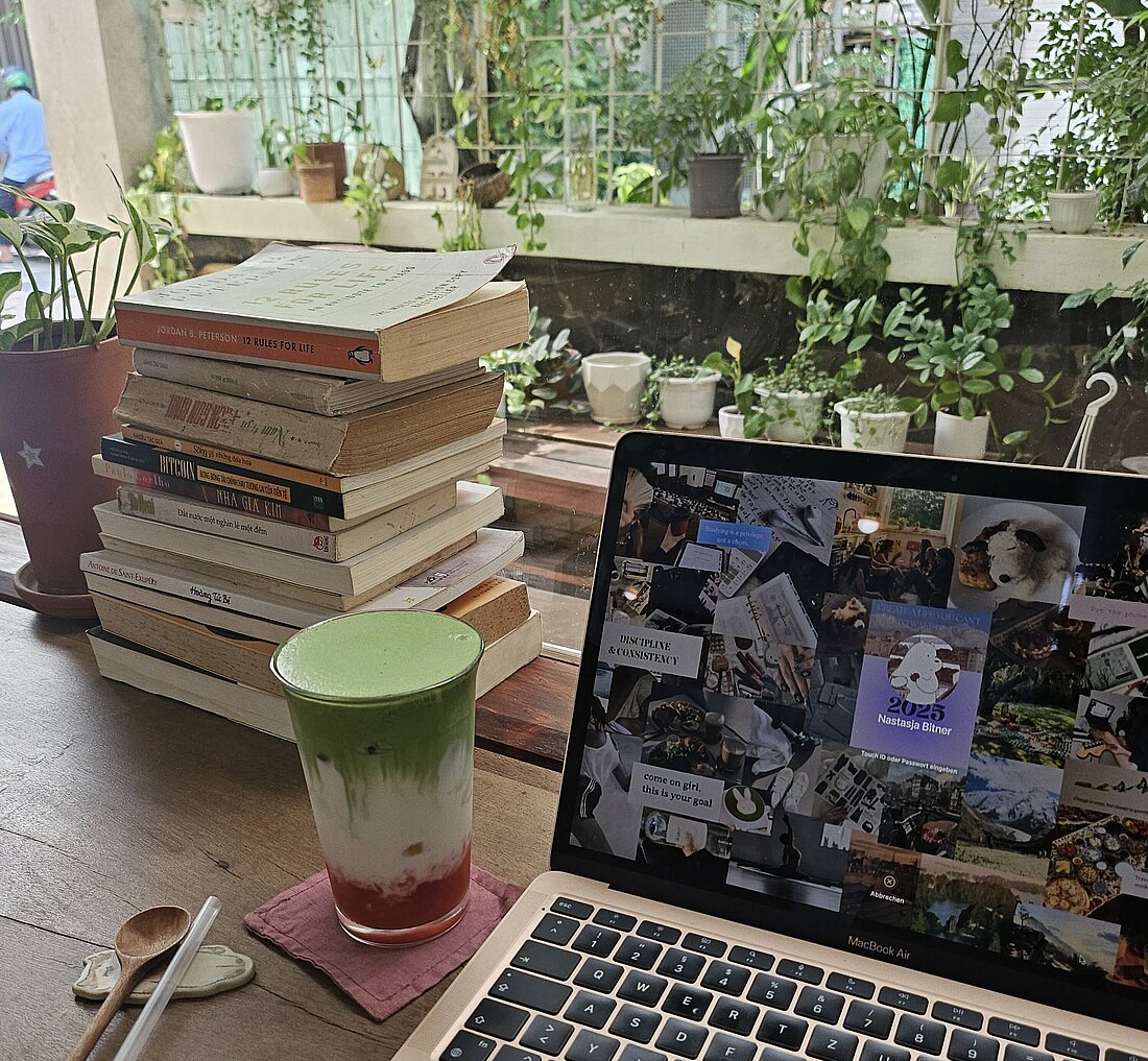Auf dem Bild zu sehen ist ein Tisch am Fenster mit geöffneter Laptop, einem Getränk und Sicht nach Draußen