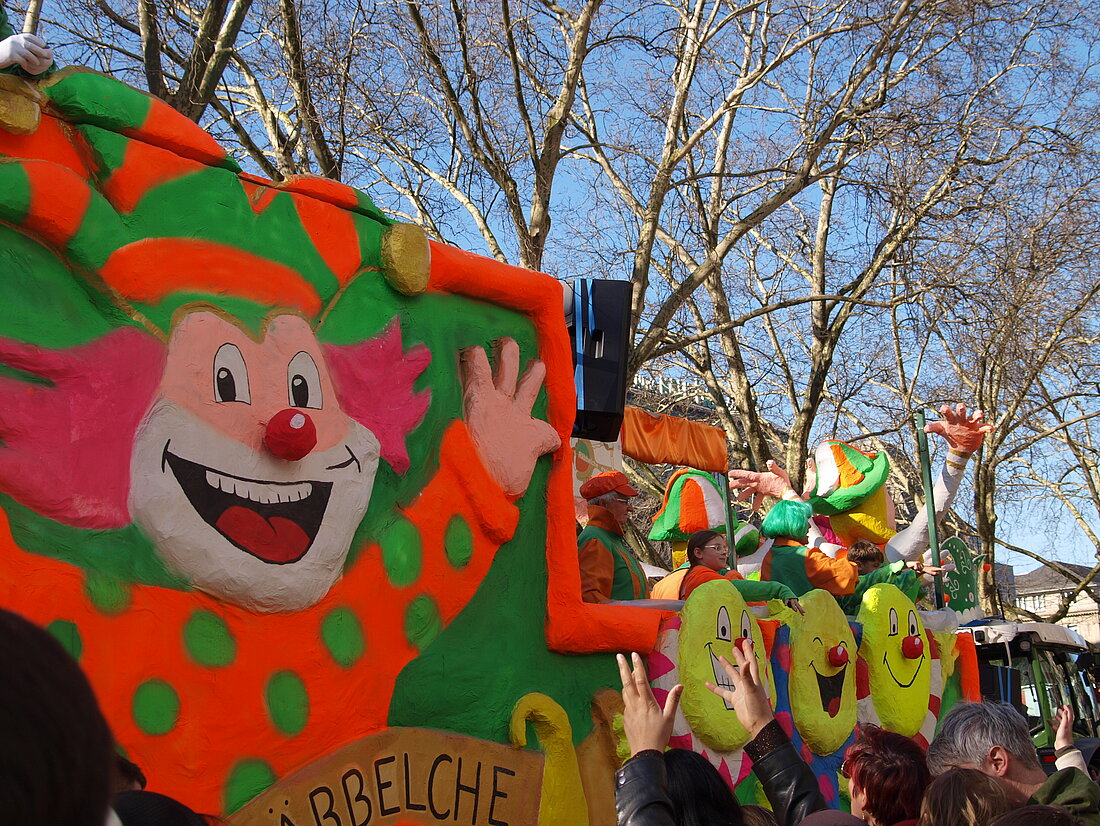 Ein Mottowagen auf dem ein großer orange-grün angezogener Clown mit roter Nase abgebildet ist.