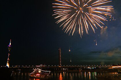 Zu sehen ist der Fernsehturm in Düsseldorf am Rhein hinter einer Brücke. Am Himmel ist ein Feuerwerk. 