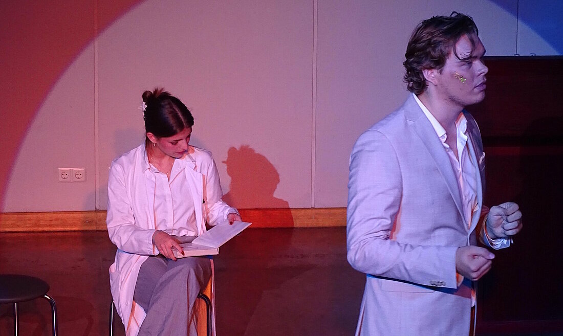 Auf dem Bild ist die Doktorin, sie ist sitzend in ein Buch vertieft, und der Erzähler, welcher von ihr weg gewandt steht, zu sehen .