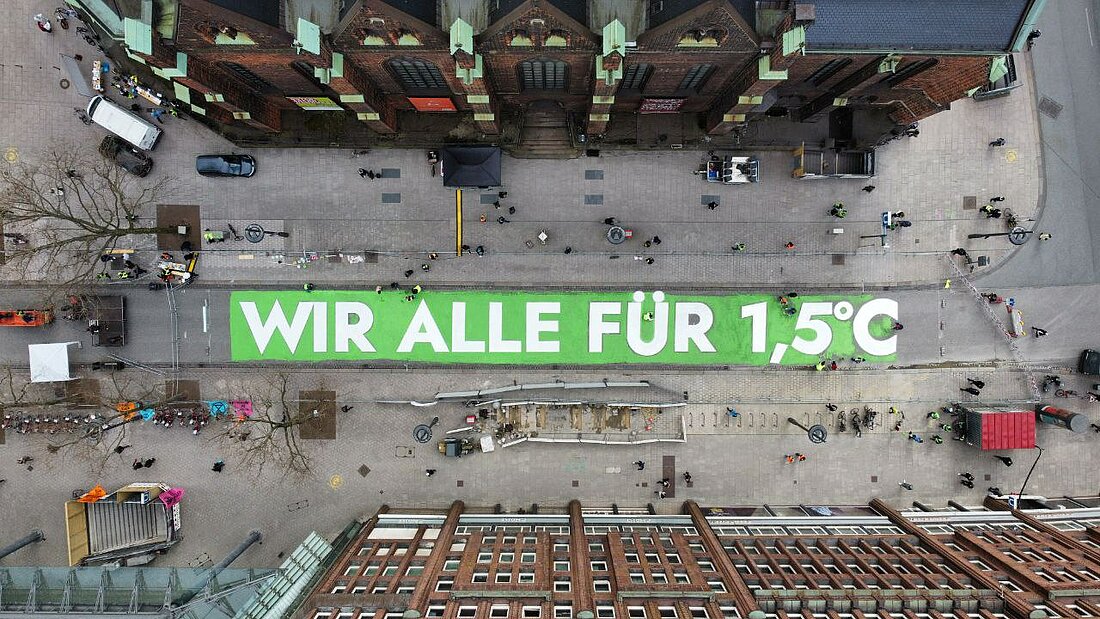 Zu sehen ist ein großer Schriftzug auf einer Straße von oben der besagt: Wir alle für 1,5.