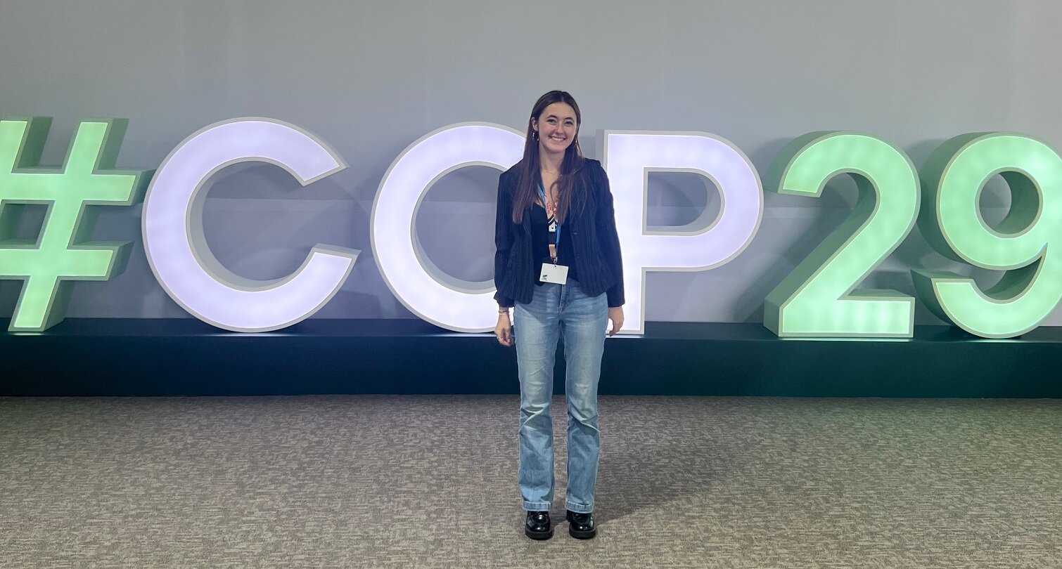 Auf dem Foto ist Yamina Probst zu sehen. Sie steht vor einem leuchtenden Schriftzug. Der Schriftzug lautet:#COP29