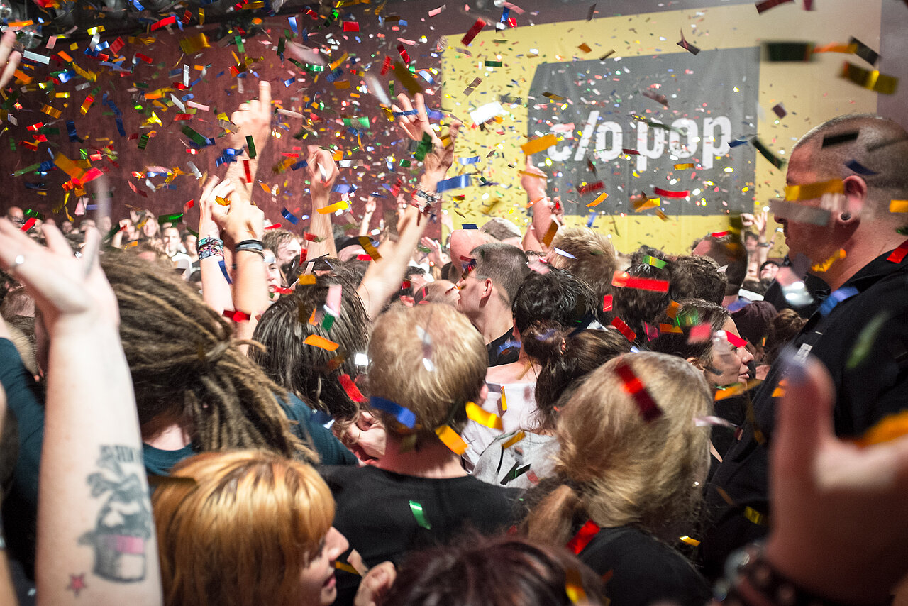 Neben dem Headliner Bilderbuch gibt es auf dem Festival vor allem Konzerte von Newcomer:innen. (Foto: c/o pop Festival / © Niclas Weber) Ein Publikum feiert mit Konfetti vor dem c/o pop Festivallogo.