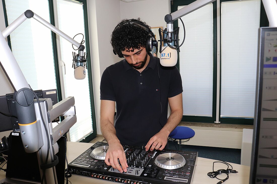 Jonaid Aydi steht hinter einem DJ-Pult. Er dreht an den Knöpfen und spielt so Musik ab.