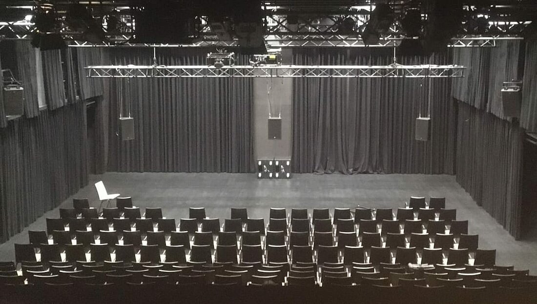 Der Saal, kurz vor Einlass. (Foto: Soundcinema Düsseldorf/Sonische Inteferrenzen e.V./ Anna Freytag) Man sieht den Saal des FFT während er noch komplett leer ist, das Bild ist ebenfalls hinter der letzten Reihe aufgenommen worden. An den Wände und der Decke sind viele verschiedenen Lautsprecher zu erkennen.