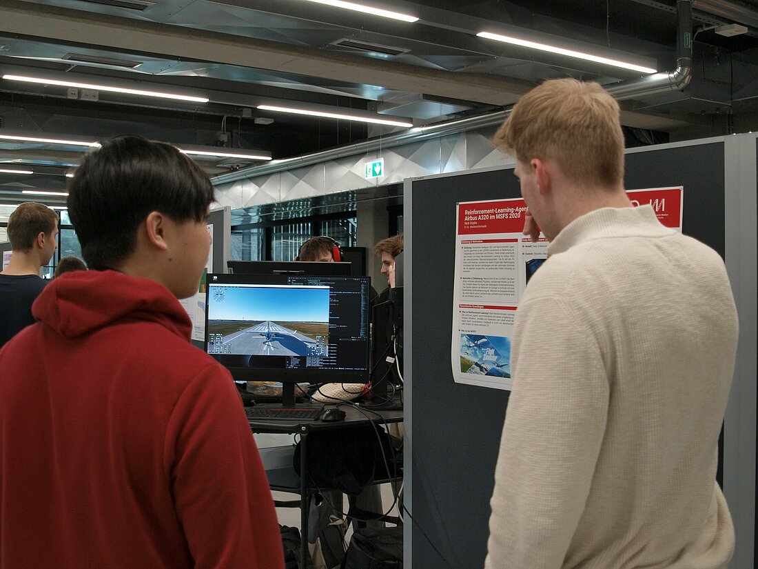 Zwei Männer unterhalten sich vor einem Laptop auf dem ein Flugsimulator zu sehen ist.