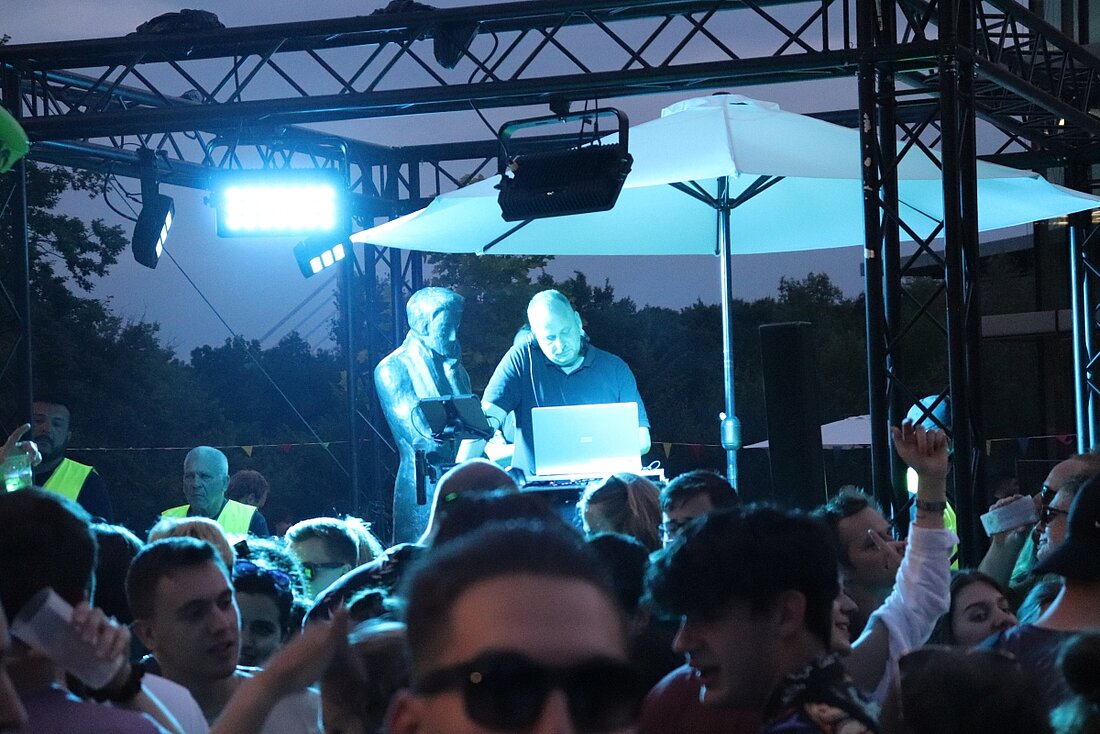 In der Mitte der Menge steht der DJ neben der Heine-Statue vom blauen Licht bestrahlt.