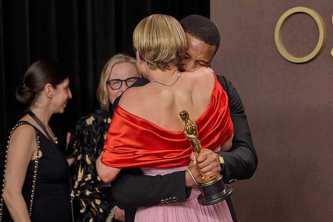 Michael B. Jordan und Jessie Buckley umarmen sich überglücklich, Jordan hält seinen Oscar fest in der Hand.