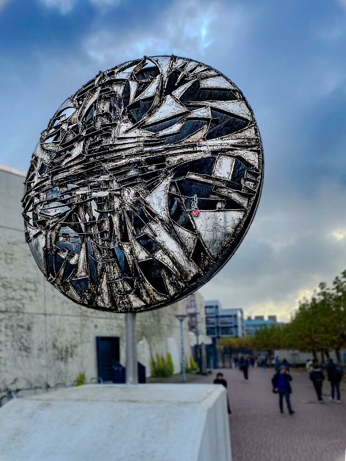 Ein Kunstwerk aus Metal auf dem Campus an welchem viele Studierende vorbei laufen.