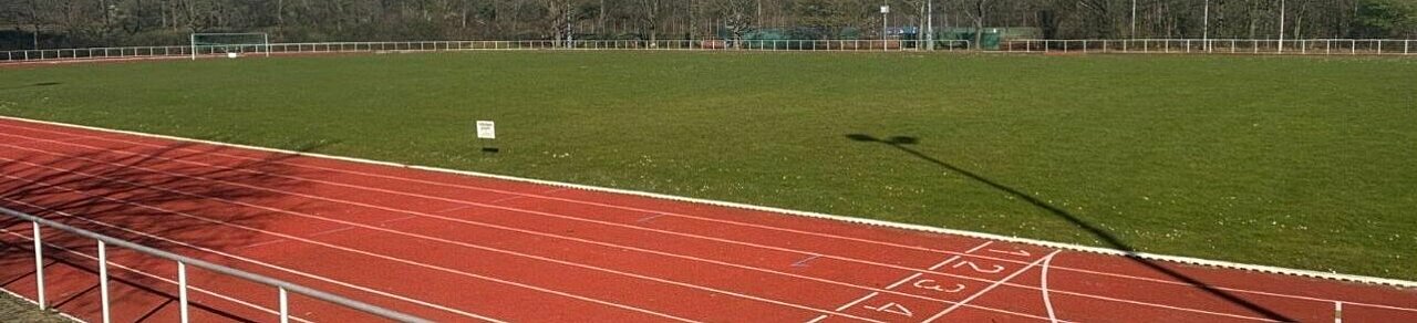 Auf dem Bild sieht man die Laufbahn der Heinrich-Heine Universität in Düsseldorf. Im Hintergrund ist der Rasenplatz mit Fußballtoren auf beiden Seiten sichtbar.