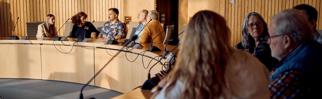 Zeigt viele Personen an einem runden Tisch, die diskutieren.