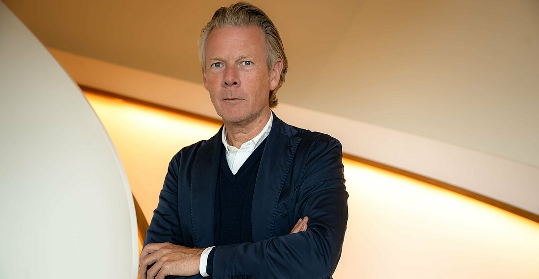 Auf dem Bild sieht man den Kurateur der Ausstellung Robert Müller-Gruenow, wie er mit verschränkten Armen in die Kamera schaut.