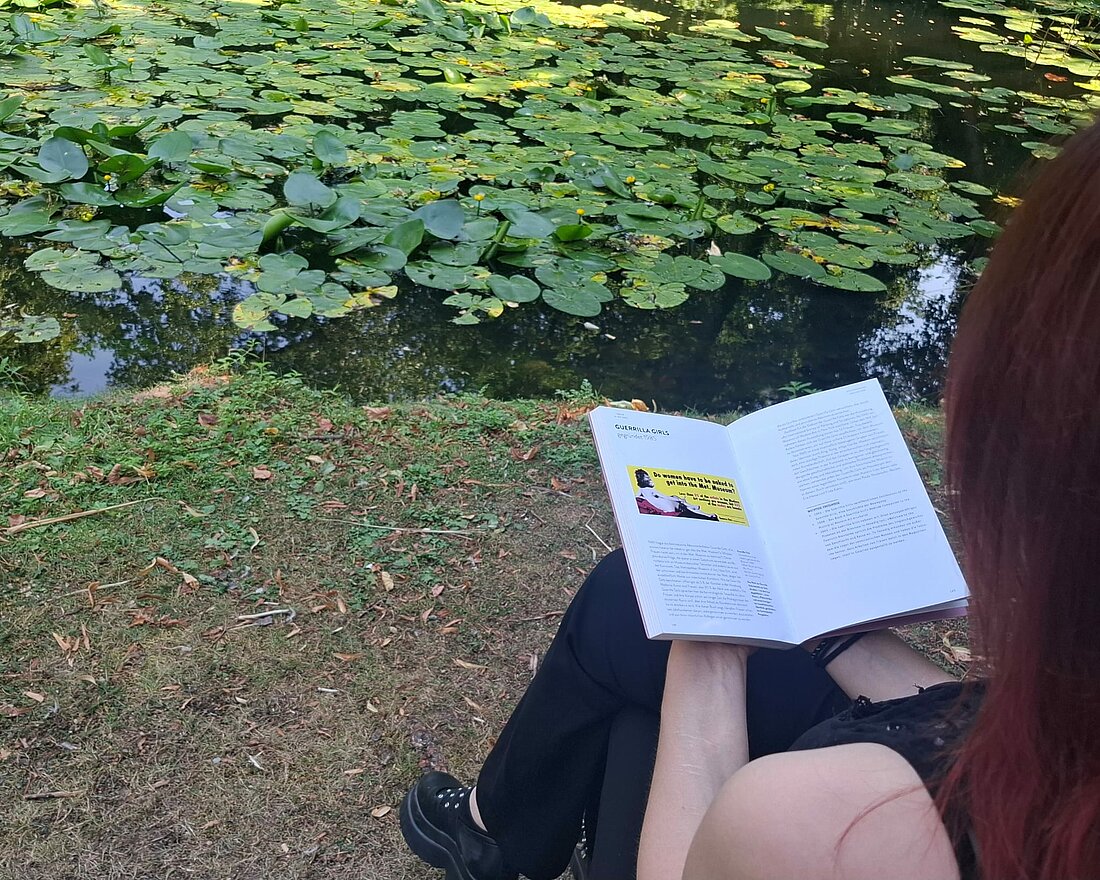 Auf dem Bild sieht man, wie eine Frau ein Buch liest auf dem man das Poster der Guerilla Girls sehen kann.