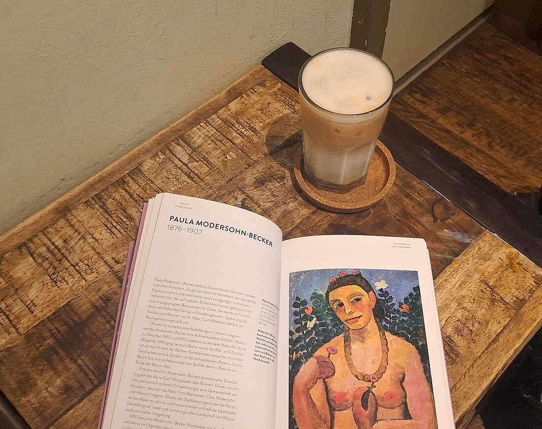 Auf dem Foto sieht man ein Buch mit einem Kunstwerk, liegend auf einem Tisch