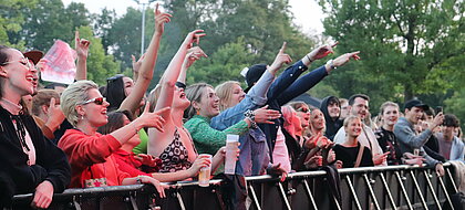 Festivalstimmung auf dem Sommerkult 2022. (Foto: Lena Berghaus) Zu sehen sind junge Menschen, die vor einer Bühnenabsperrung stehen und singen und tanzen
