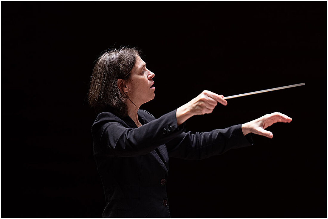 Auf dem Bild sieht man die Dirigentin Silke Löhr im Closeup mit erhobenem Taktstock.
