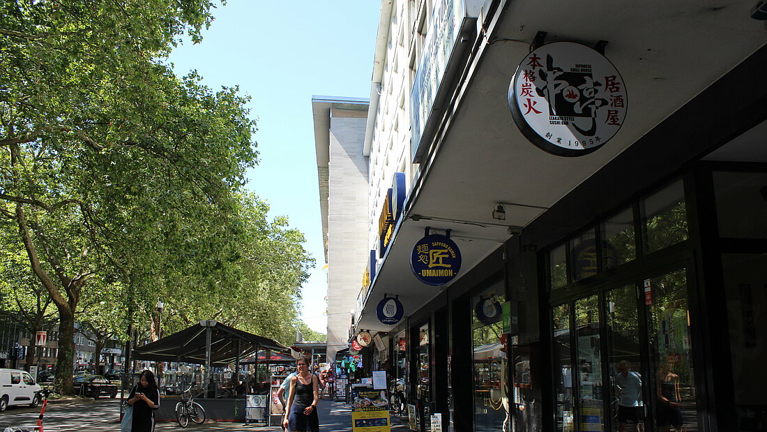 Ein Blick die Immermannstraße runter mit Personne die einem entgegen kommen und den runden Schildern der Japanischen Lokale