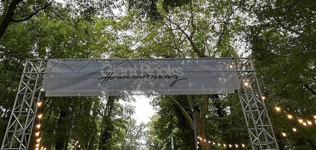 Man sieht ein Banner mit der Aufschrift Giant Rooks Homecoming zwischen zwei Stahlsäulen. Eine Lichterkette zwischen den Bäumen erzeugt eine gemütliche Stimmung.
