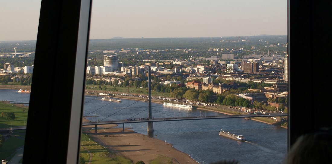 Auf dem Foto sieht man den Blick aus dem Rheinturm bei gutem Wetter. Man sieht die Rheinbrücke und den Rhein sowie die Innenstadt.