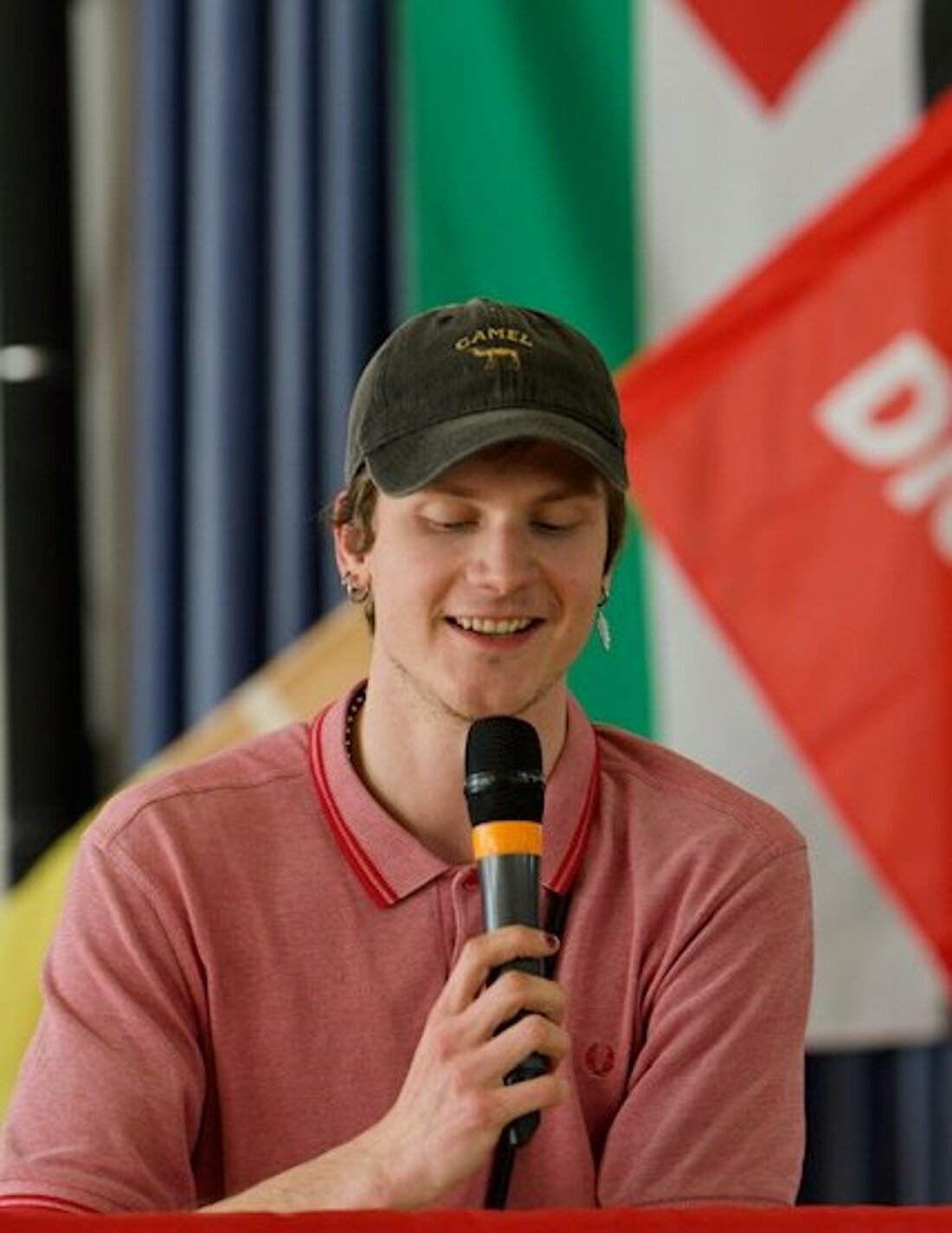 Maxi Kisters spricht in ein Mikrofon, hinter ihm sind Palästina-Flagge und ein Banner Der Linken zu sehen.