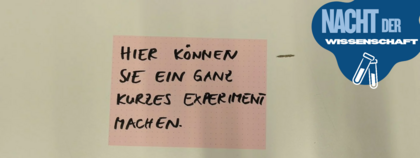 Auf dem Bild ist ein Zettel zu sehen. Auf dem Zettel steht „Hier können Sie ein ganz kleines Experiment machen“.