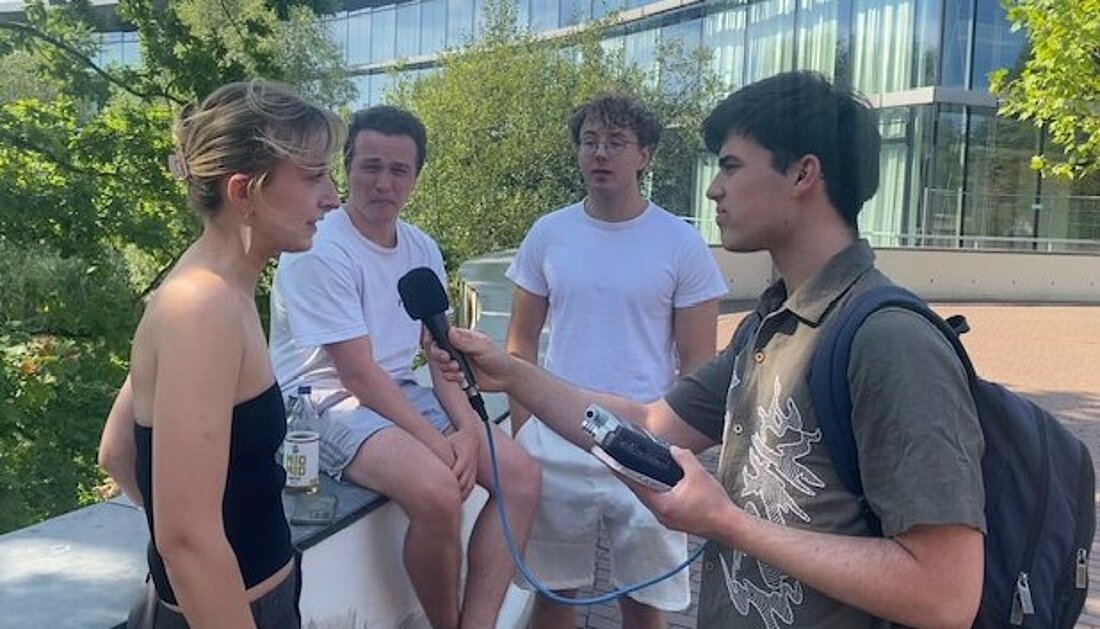 Auf dem Bild sieht man drei Studierende auf der Mauer sitzen und sie werden von Pedro vom hochschulradio düsseldor interviewt