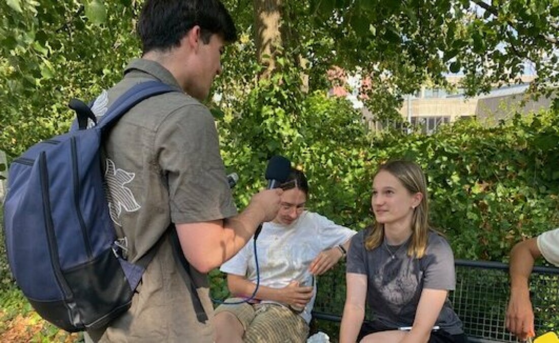 Auf dem Bild sieht man eine sitzende Frau, die von hochschulradio düsseldorf interviewt wird auf dem Campus